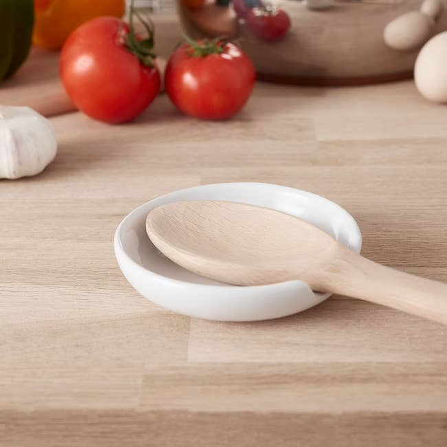 Wooden spoon rests connected  a achromatic  ceramic dish, surrounded by caller  vegetables and room  items, suggesting a cooking oregon  room  buying  theme