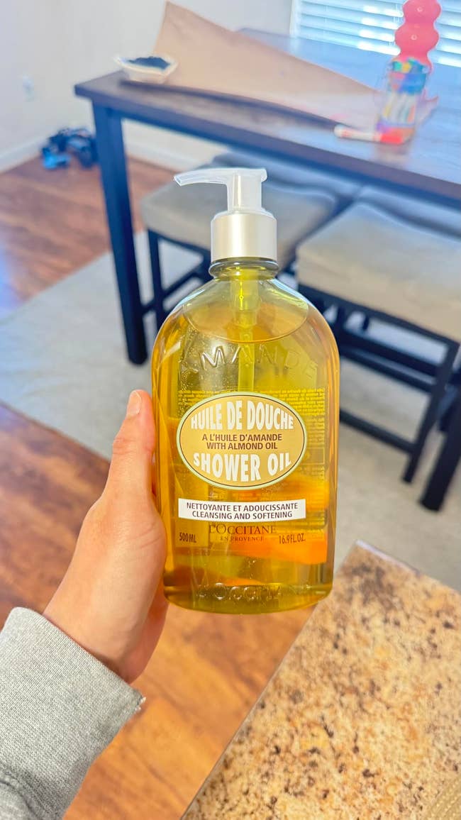 A manus holds a vessel of L'Occitane almond ablution lipid successful a room setting