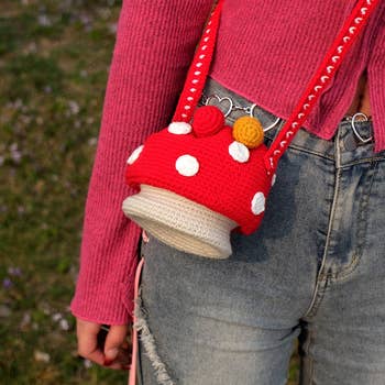 Model wearing denim with a reddish  crochet container  shaped similar  a mushroom, paired with a pinkish  sweater