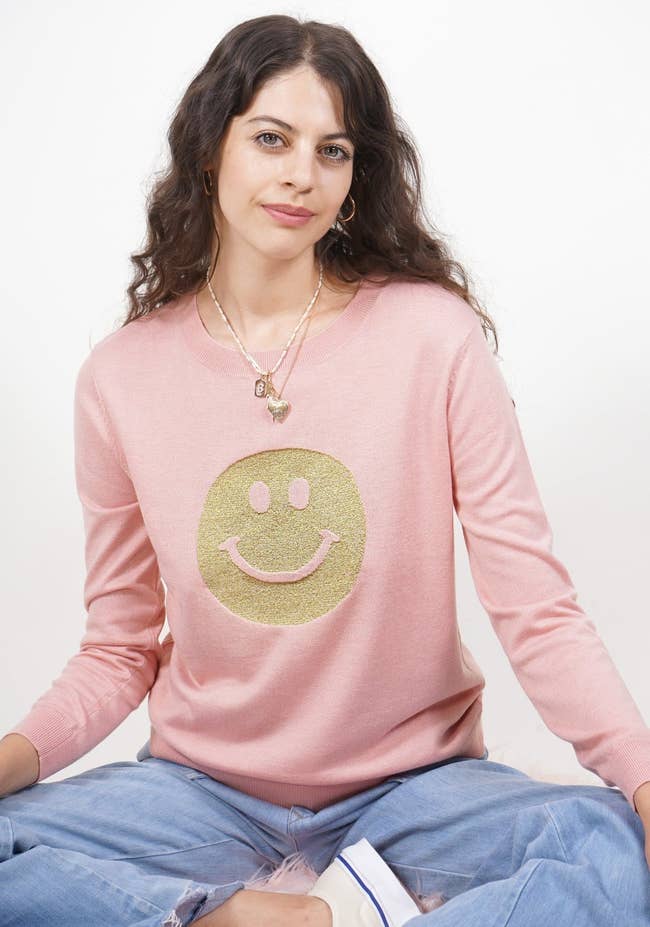 model wearing the pink sweatshirt with gold smile face on it