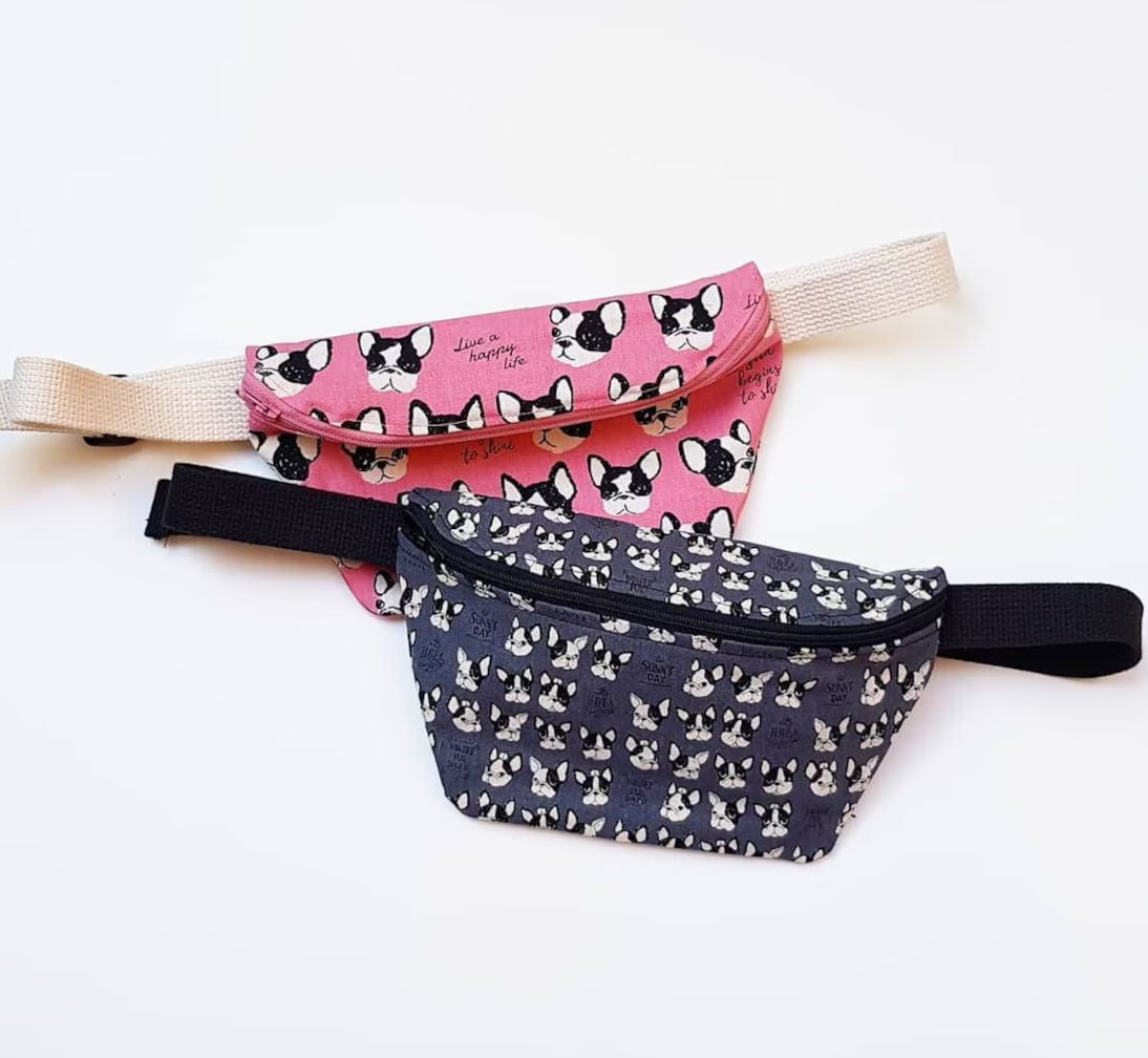 Pink fanny pack with illustration of black and white French Bulldog heads underneath product in navy with smaller illustrations of dog heads