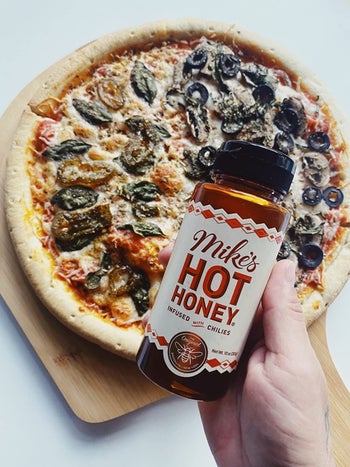 reviewer holds bottle of Mike's Hot Honey over veggie pizza