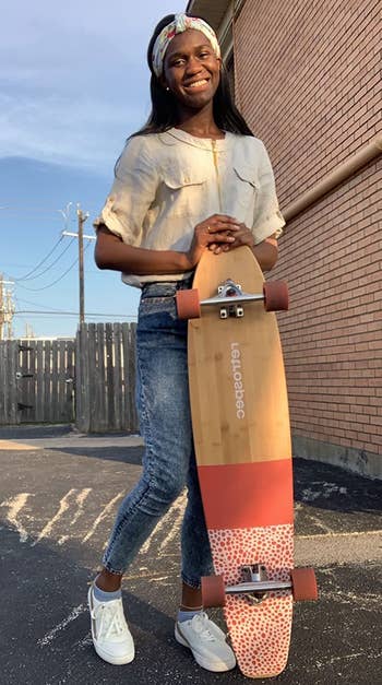Reviewer standing next to a longboard in a bamboo and pink color