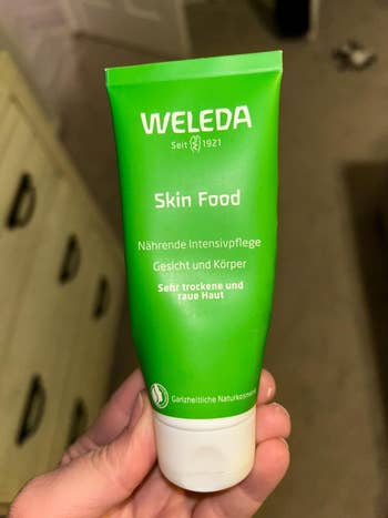 Hand holding a tube of Weleda Skin Food cream for dry and rough skin