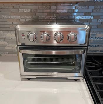 Stainless alloy  countertop convection oven with 4  power  knobs and a wide   beforehand   door, placed beside a stove connected  a room  counter