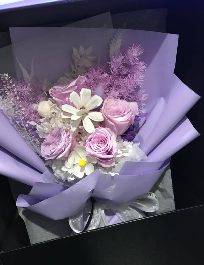 Bouquet with roses and assorted flowers wrapped in purple paper, placed in a box. Ideal for gifting