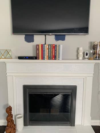 A wall-mounted TV supra a fireplace with a mantel displaying books, decorative items, and candles