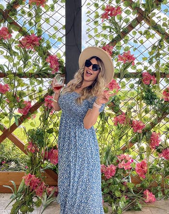 a different reviewer wearing the dress in blue with straw hat while holding wine glass