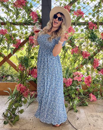 a different reviewer wearing the dress in blue with straw hat while holding wine glass