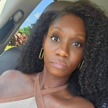 Reviewer in a car with hoop earrings and a one-shoulder top, looking at the camera