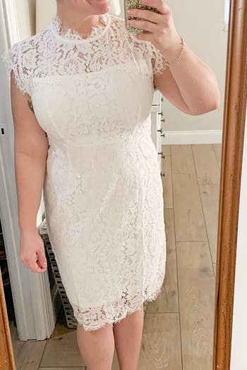 Reviewer wearing lace knee-length dress with high neckline and shortsleeves in front of wood frame wall mirror