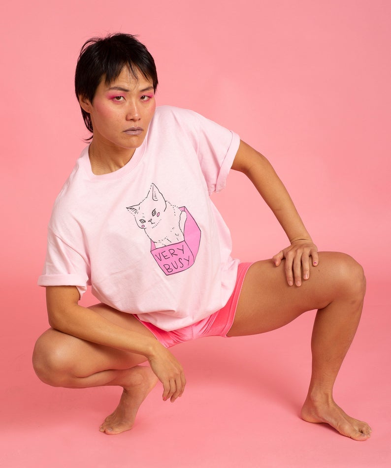 model wearing pink short sleeve tee with illustrated cat sitting in a box that reads
