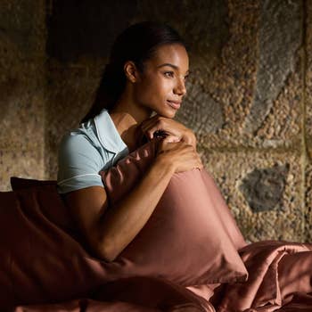 A idiosyncratic sits connected a bed, holding a pillow, appearing relaxed and contemplative. The mounting suggests a cozy, inviting chamber environment