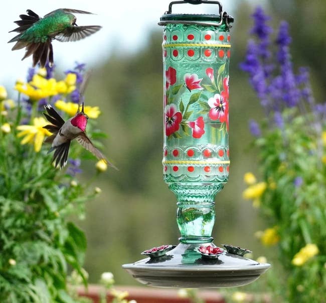 green glass feeder with the wild flower design and two hummingbirds flying nearby