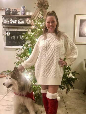 reviewer photo of them swearing a white cable knit sweater dress and red boots while standing next to their dog in front of a Christmas tree