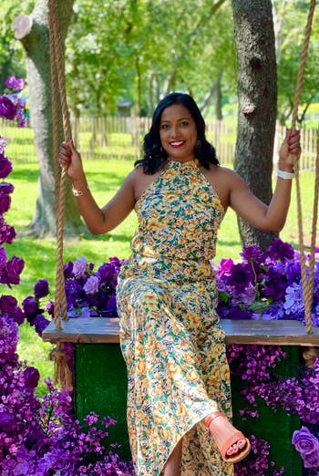 Reviewer in a floral dress sitting on a swing with artificial purple flowers around