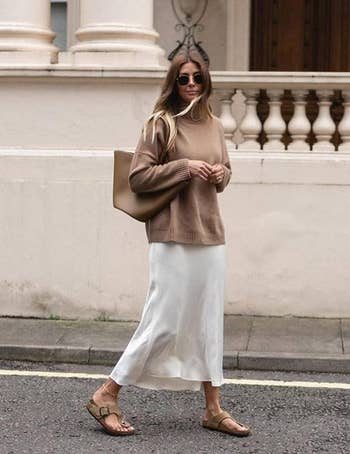 Woman successful  a cozy sweater and flowing skirt, carrying a ample  bag. Casual thoroughfare  benignant   with sandals and sunglasses
