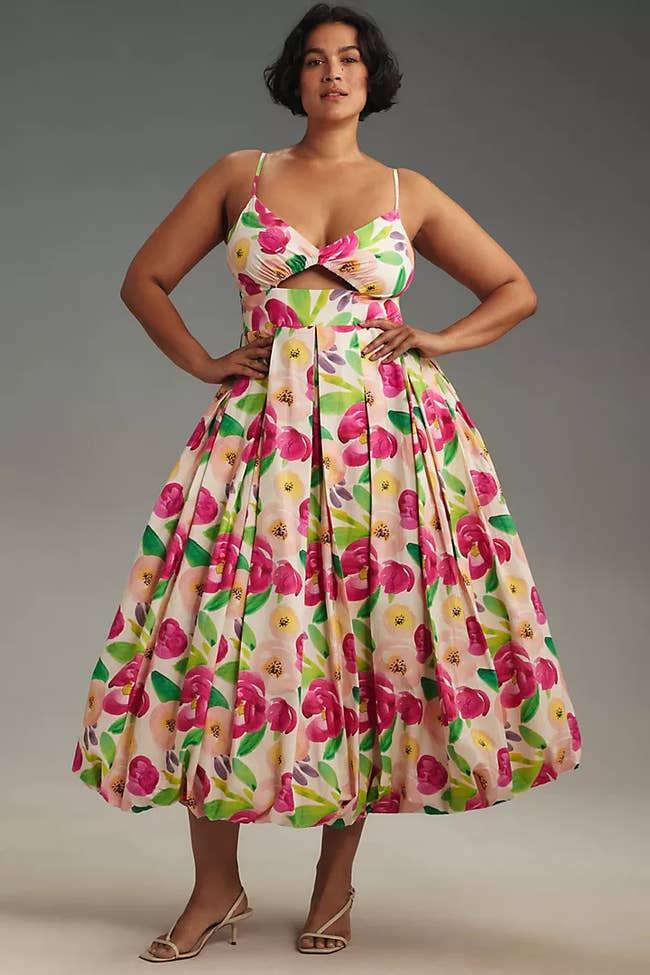 Woman in a floral print dress with a full skirt and spaghetti straps, posing for a shopping article