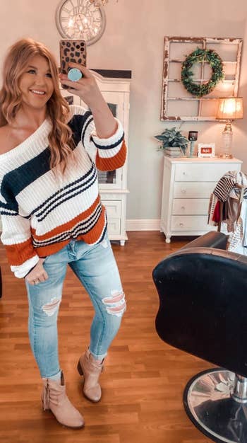 reviewer wearing the white, black, and orange striped sweater with jeans