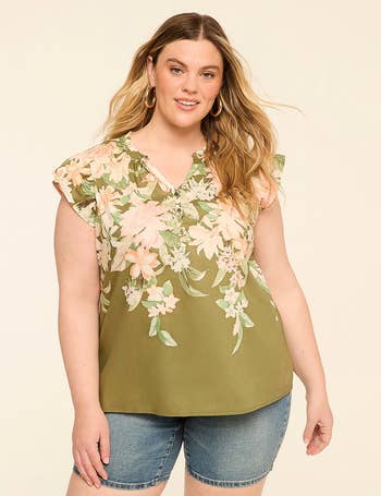 Woman wearing a floral blouse with ruffled sleeves and denim shorts, posing confidently for a manner  shoot