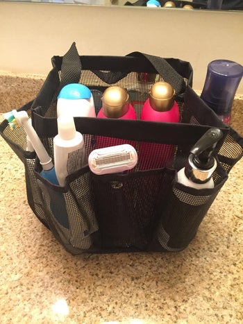 pic of mesh black shower caddy filled with shampoo, conditioner, and soap bottles and shaving supplies