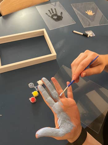 Person applying paint on their hand for handprint art, with art supplies on table