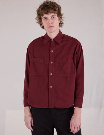 Person wearing a maroon button-up garment  with beforehand   pockets