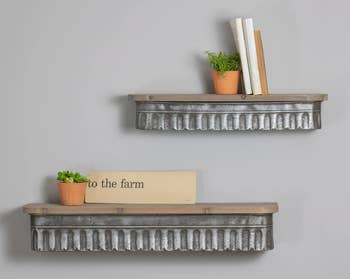 Two wooden and silver distressed floating shelves on a wall with two plants and books on top