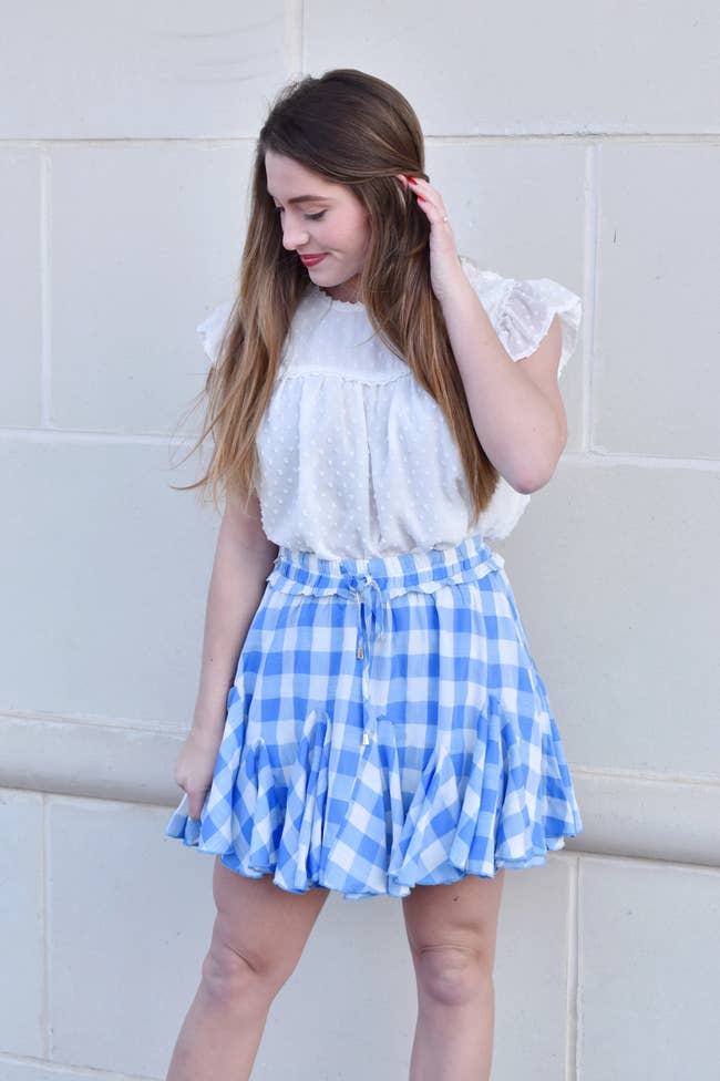 Model is wearing a white top and a blue and white gingham skirt