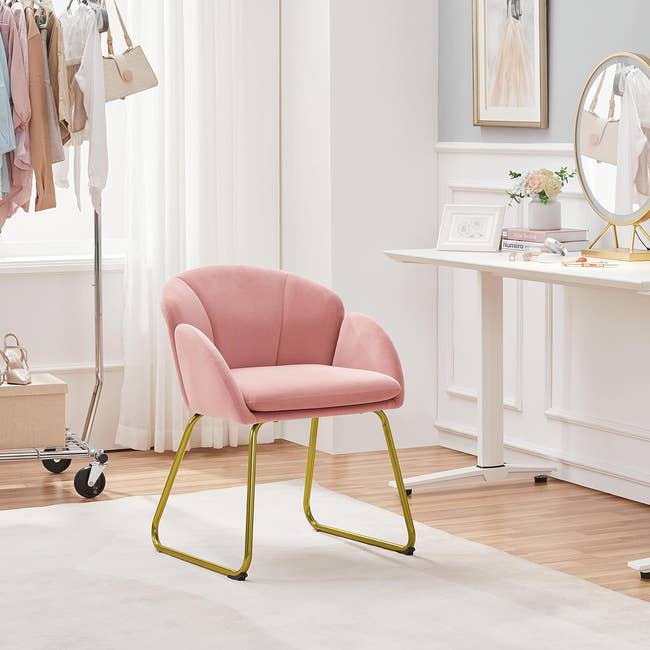 Pink chair with gold legs in a bright, modern bedroom set-up, adjacent to a vanity. Ideal for chic home decor