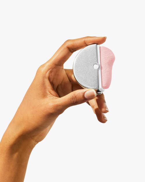 Hand holding a small, semi-circular device with a pink pad, likely a facial exfoliator or beauty tool, suitable for skincare routines