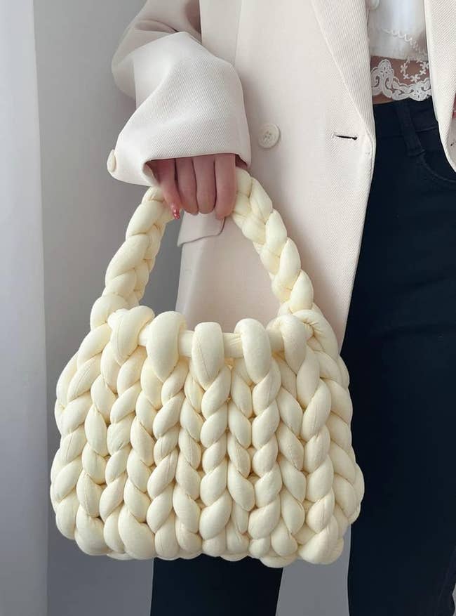 Model holding white chunky knit handbag by the single handle 
