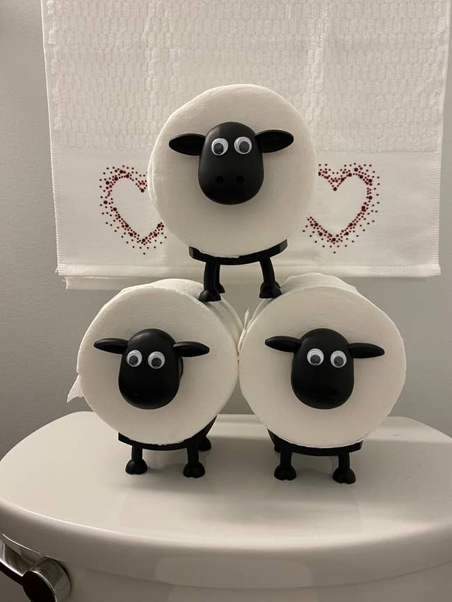 Three toilet insubstantial rolls are stacked connected sheep-shaped holders connected a toilet tank. A towel with bosom designs hangs successful the background