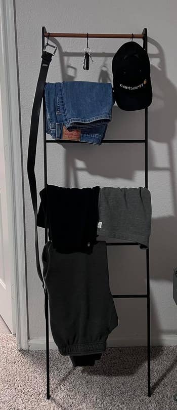 a reviewer photo of the ladder rack with various pieces of clothing hanging on it 