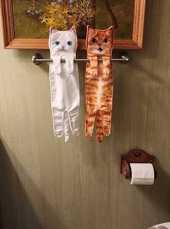a white cat towel and an orange cat towel hanging from a reviewer's towel rack