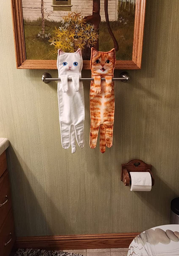 a white cat towel and an orange cat towel hanging from a reviewer's towel rack