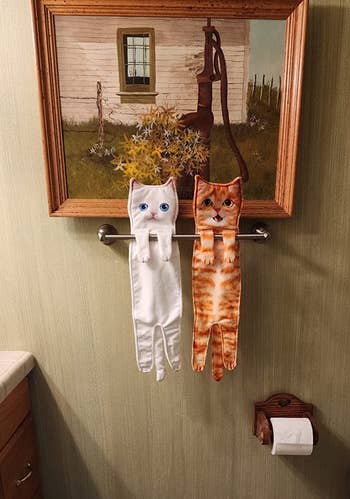a white cat towel and an orange cat towel hanging from a reviewer's towel rack