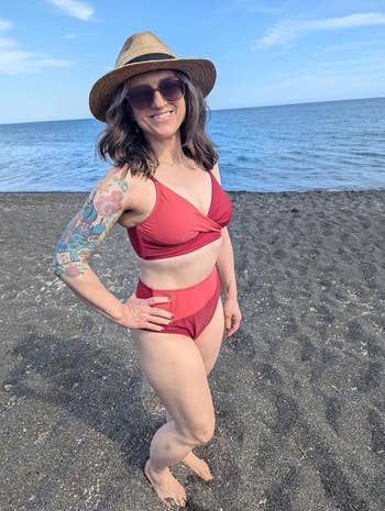 Person connected  a formation  wearing a hat, sunglasses, and a two-piece swimsuit with tattooed arm. The inheritance  shows soil  and a calm sea