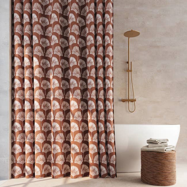 Bathroom with a patterned ablution curtain, a freestanding bathtub, a modern ablution fixture, and a woven handbasket with towels