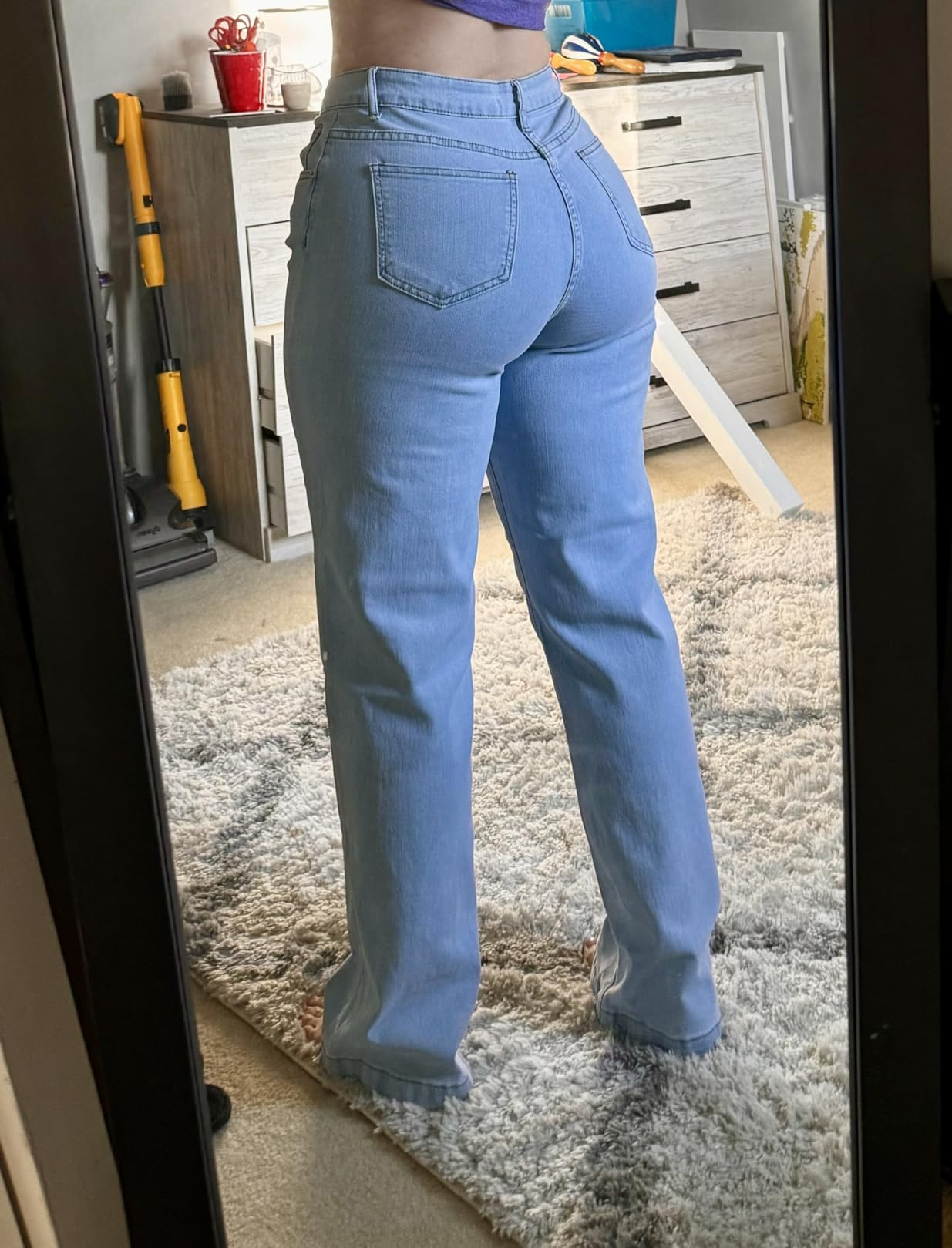 A idiosyncratic   wearing straight-leg jeans stands successful  beforehand   of a mirror, showcasing the acceptable  from the back, successful  a country   with location  items visible