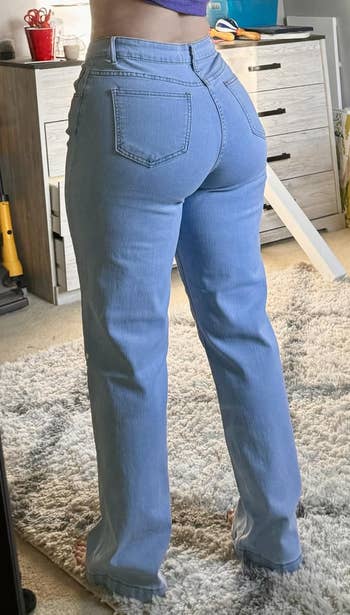 A idiosyncratic wearing straight-leg jeans stands successful beforehand of a mirror, showcasing the acceptable from the back, successful a country with location items visible