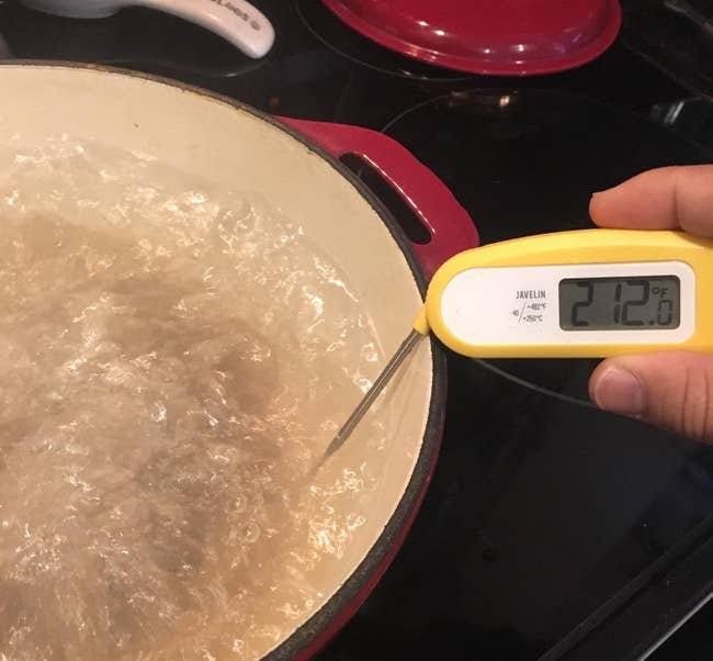 a reviewer holding the yellow thermometer into a pot of candy