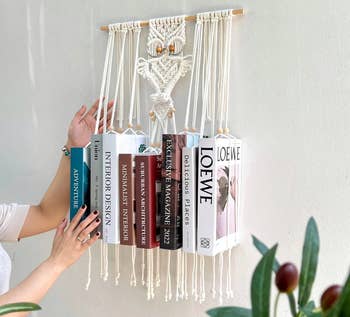 Macrame publication holder displaying six books connected plan and architecture. A person's hands are adjusting the books