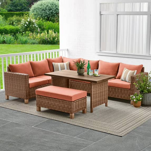 Outdoor patio acceptable with wicker seating, orangish cushions, a rectangular table, and a rug connected a porch, acceptable against a plot backdrop
