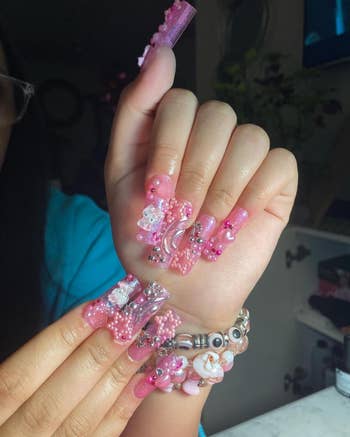 a reviewer's nails covered in pink nail art charms