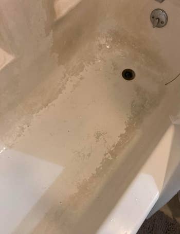 A bathtub with signs of wear, including peeling and cracks successful the surface, adjacent the drain and faucet area