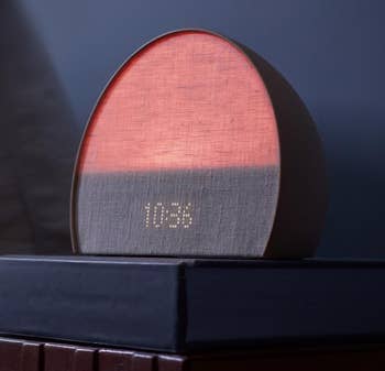 An alarm clock glowing soft red light with a fabric-covered digital display showing the time 