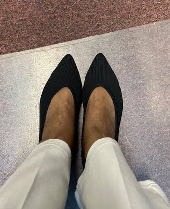 Person wearing achromatic pointed-toe heels paired with light-colored pants connected a textured surface