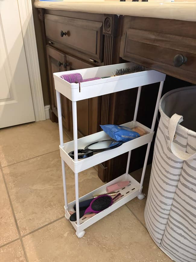 Bathroom with a achromatic  rolling retention  cart holding combs, brushes, and idiosyncratic   attraction   items adjacent  to a laundry basket