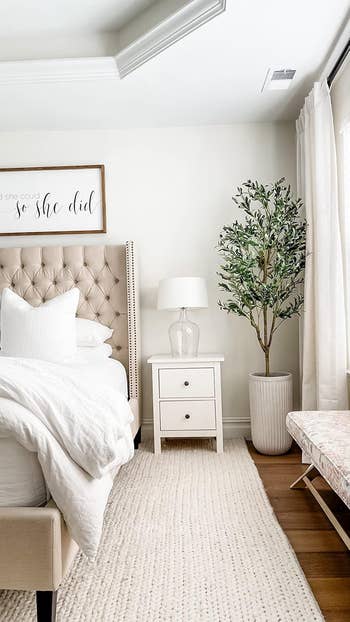 Minimalist chamber  with a tufted bed, achromatic  linens, a bedside array  with a lamp, a ample  potted plant, and a motivational partition  sign